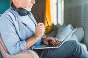 close-up-de-homem-segurando-oculos-usando-computador-portatil